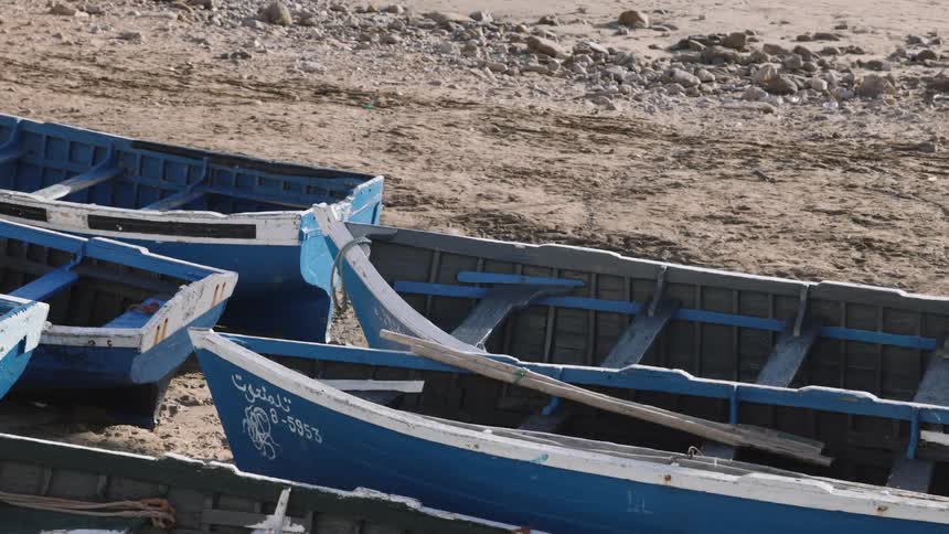 Several blue wooden fishing boats are parked close together on a sandy rocky shorethe boats feature white trim and some have writing or identification numbers visible on their sides