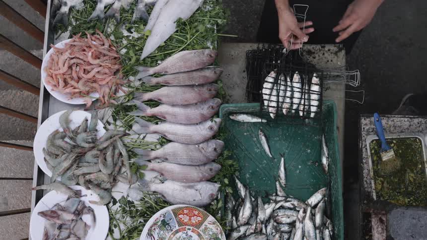 Stylized outline of a fish positioned just to the right of the green crate containing small silver fish a similar vertical fish outline located slightly further to the right and lower down near the edge of the table