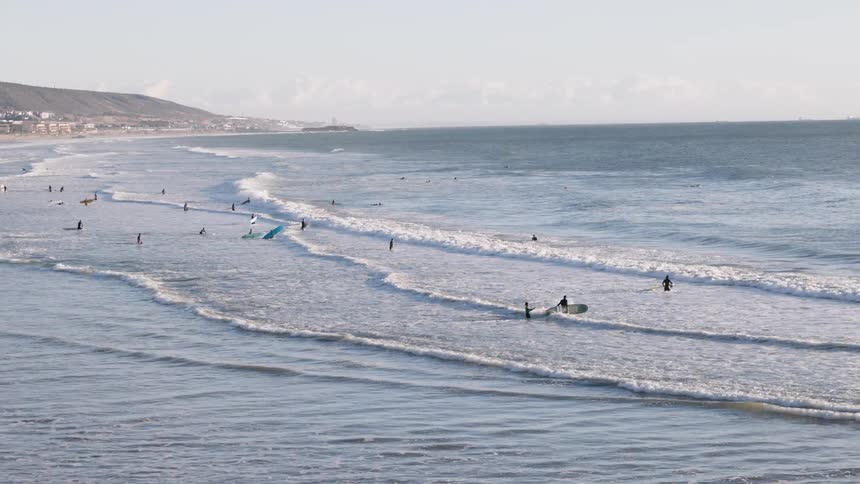 Surfers wade in ocean waves near the coastline on a partly sunny day