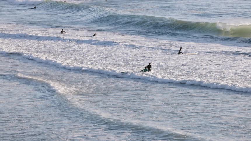 Surfers wait for waves in the ocean with boards spread across the breaking zone