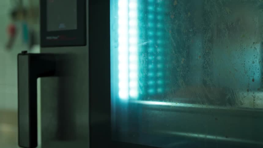 A bluelit stainless steel oven door glows through fogged glass