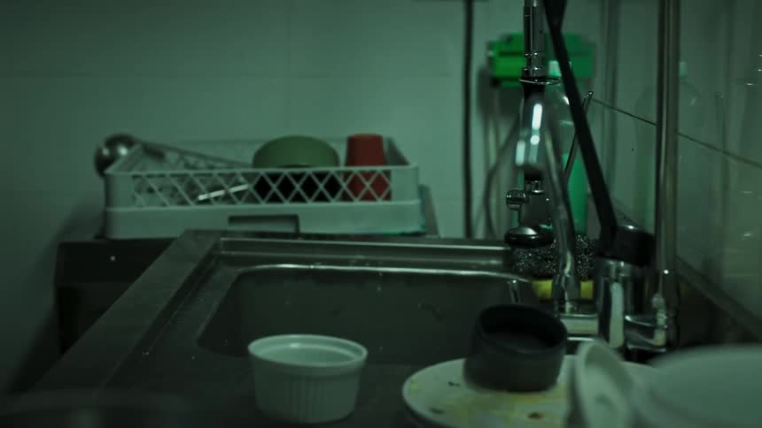 A man takes dirty dishes from a sink and puts them into a basket