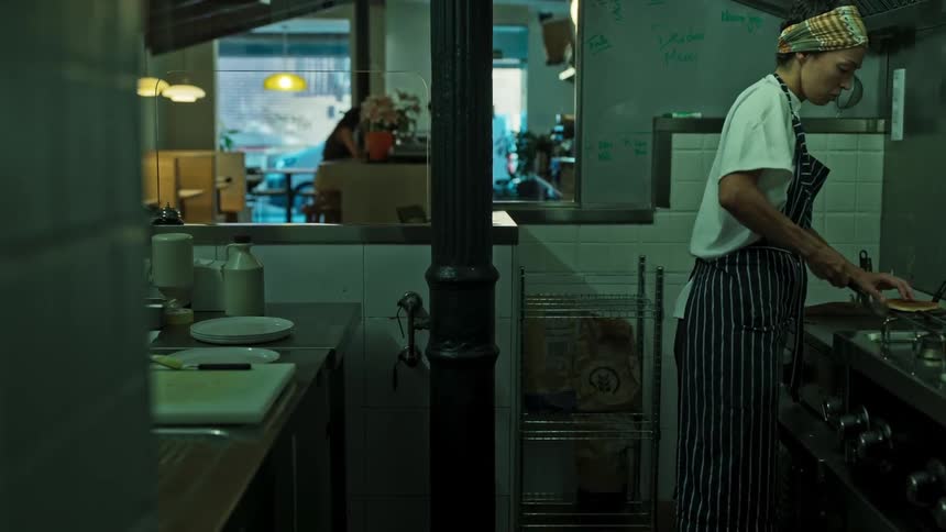 A young woman with a bandana in her head cooking something on an oven and then putting it into a plate