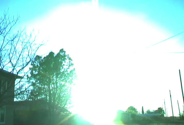 Sun glares from the horizon across a field separating houses from a field of cacti on a winter day