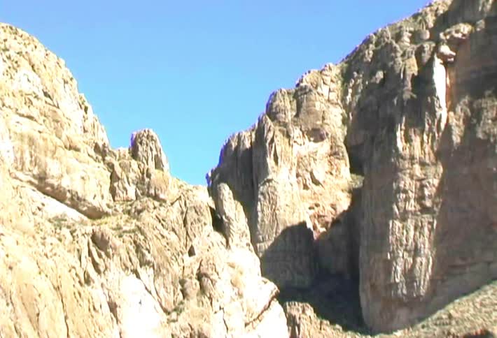 Bare stone mountains tower over a stream on a sunny day