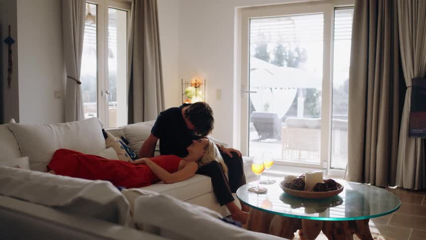 Man kisses the woman lying with her head on his lap as he sits in the living room during the daytime