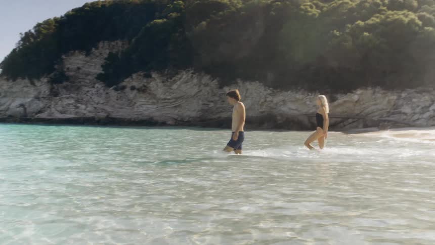 Two people walk through shallow seawater near a rocky cove