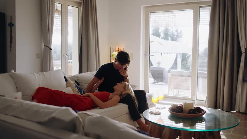 Woman lying with her head on her boyfriends lap as he sits on the couch as he bends down to kiss her