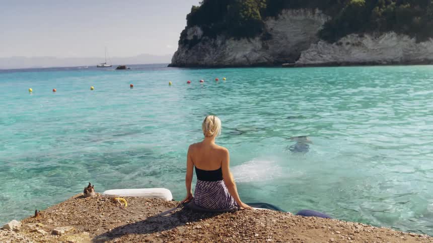 Woman sits along the coast as the man with her dives into the water