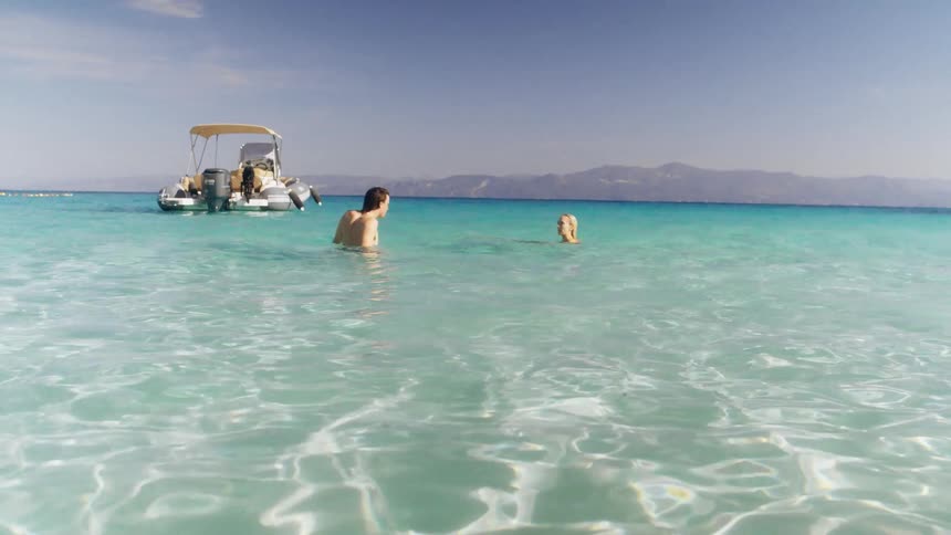 A man and woman swim near their boat on an ocean coast