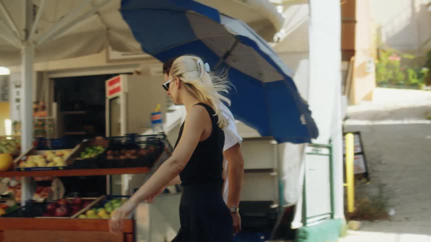 Man and woman walk on a neighborhood street past a produce stand