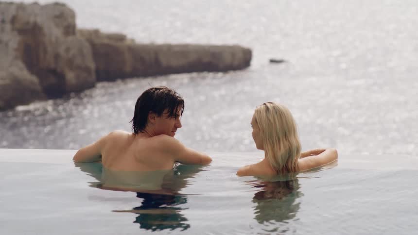 Man and woman standing together in a pool off the coast as they talk