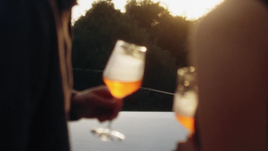 A young couple standing outdoors at sunset holding glasses of wine in front of a lake