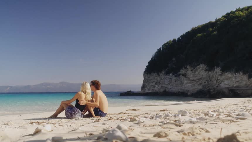 Couple sitting on the beach cuddles while looking at the ocean