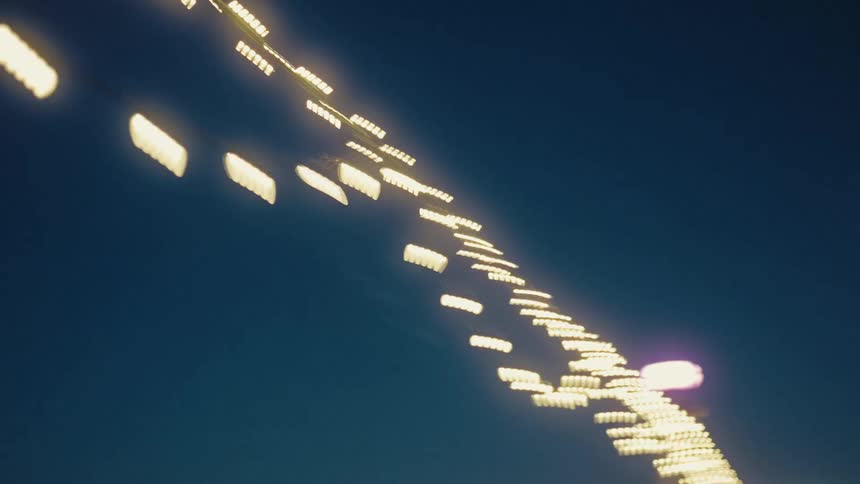 Strings of warm white lights hang against a dark blue evening sky swaying slightly as the camera pans upward to show the glowing bulbs flickering and blurring against the deep twilight background