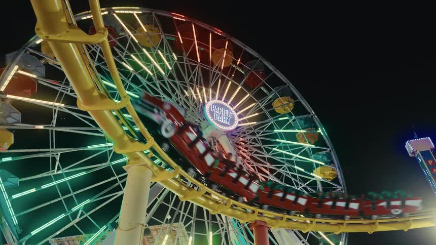 Roller coaster passes in front of a lit ferris wheel at an amusement park at night
