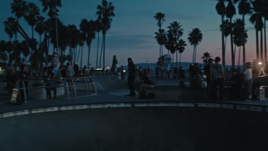 People enjoy skateboarding or standing and watching at a park after dusk