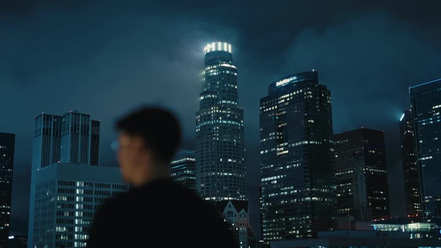 Blurred person in the foreground facing illuminated skyscrapers at night in an urban area