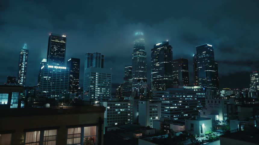 Lights glow on downtown buildings at night under a cloudy sky