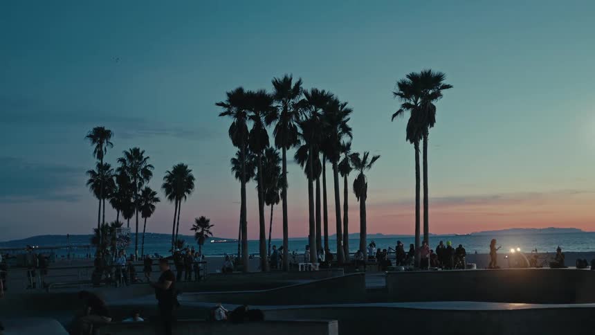 People skateboard in a busy park after dusk