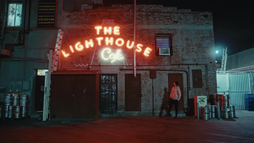 Man leaning against one of the doors of a cafe at night walks away after looking at its brightly shining sign