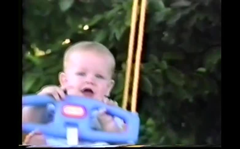 Toddler smiles while swinging in a baby swing outdoors on a summer day