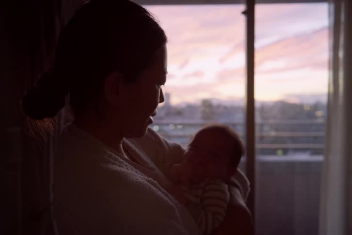The mother rocks her baby by the window