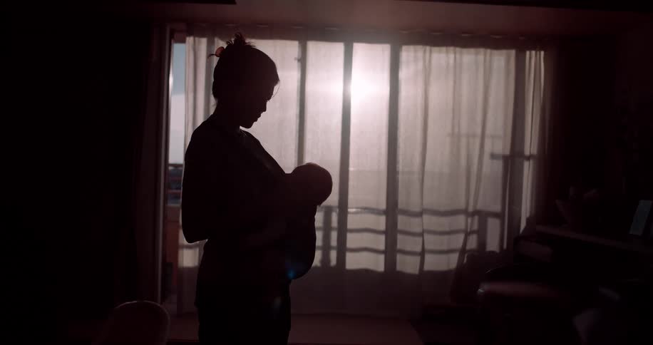 Silhouetted woman holds her infant while standing at home on a sunny day