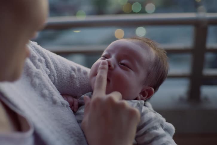 Adult holds a baby in their arms and gently touches the childs nose in an elevated outdoor setting