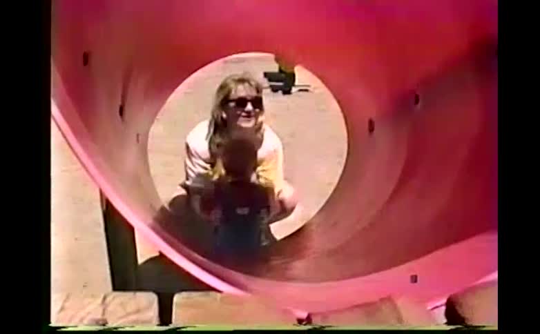 Crouching mother stands after catching her son when he has slid down a slide