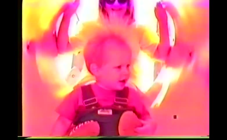 A woman laughs at the hair of a young boy sitting on a slide