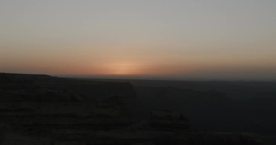A rocky coastline at sunset with a wide landmark visible on the horizon