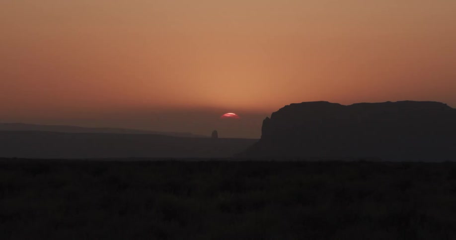 Sun setting behind rock formations with silhouetted outlines on the horizon