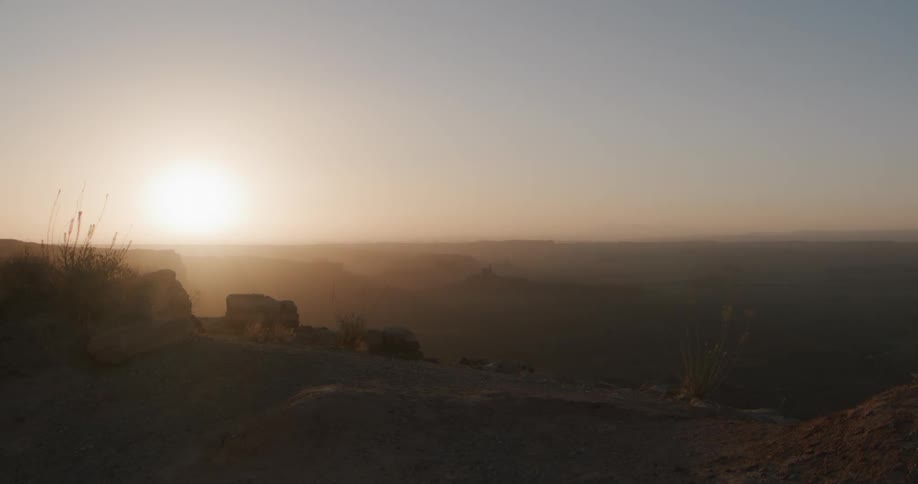 A bright sun glows through a hazy sunrise over a vast canyon landscape
