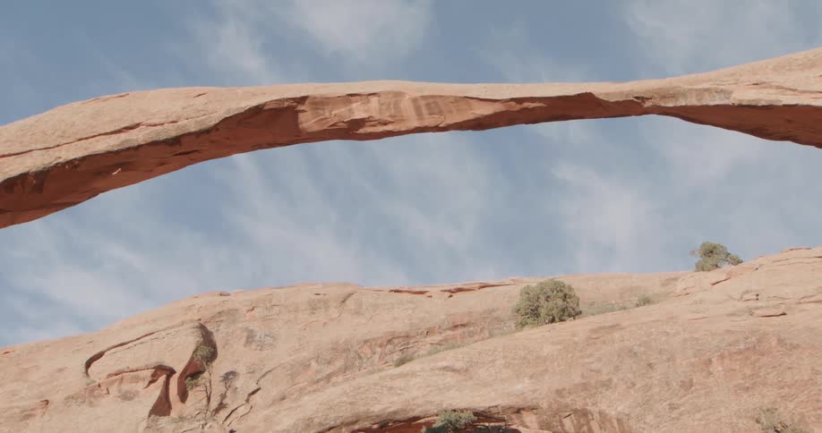 Extended natural rock arch over arid terrain with sparse vegetation