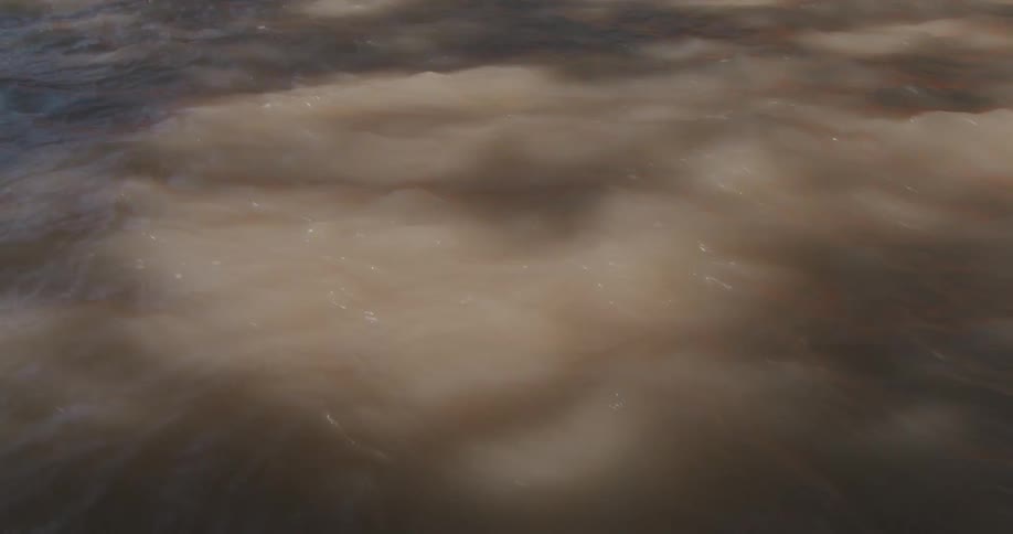 Sunlight casts shadows onto fast moving murky water during the daytime