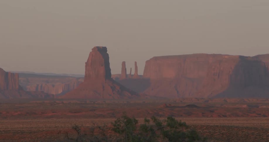 Towering red sandstone mesas stand over desert plains at dusk