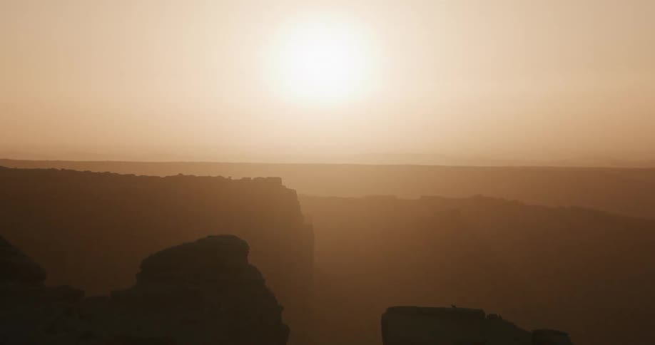 Sun shines through a cloudy sky over desert mountain canyons