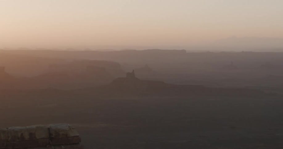 Vast desert landscape with layered terrain under soft light on the horizon