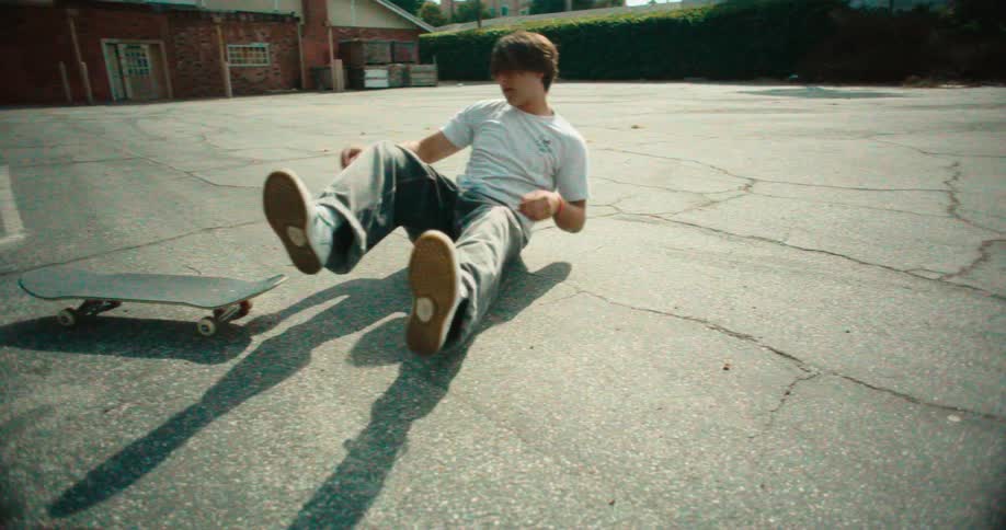 Person losing balance while falling off a skateboard on an asphalt surface