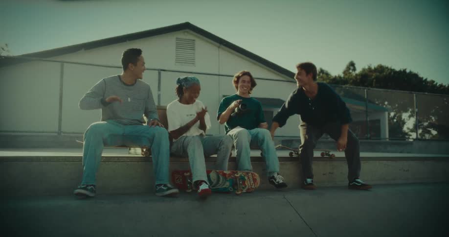 Skateboarders sitting in a skate park cheer happily then get up and run forward