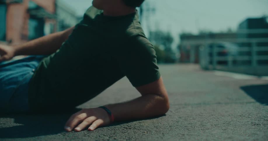 A close view of a man in a green tshirt falling onto an asphalt surface outdoors during the day