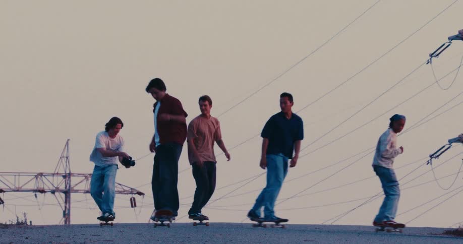 Group of friends skateboard over a road on a hill passing near electrical transmission towers on an autumn day