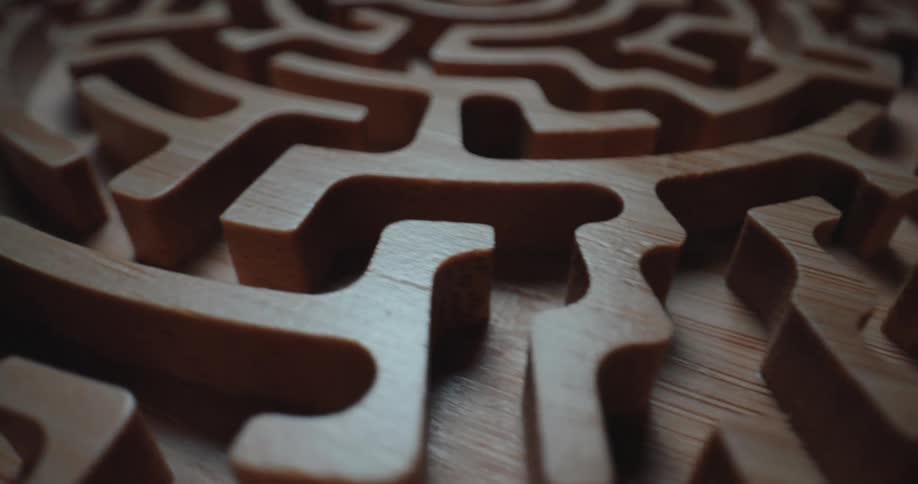 A classic wooden labyrinth maze game in a dark room with light reflecting off the wood