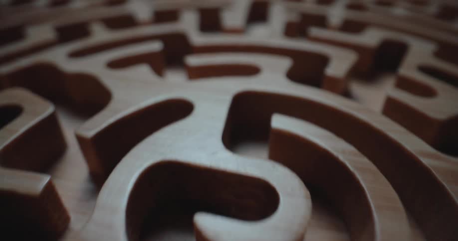 A camera pans across a detailed circular maze carved from lightcolored wood showcasing the smooth walls and narrow paths of the labyrinth under soft lighting that casts shadows on the maze
