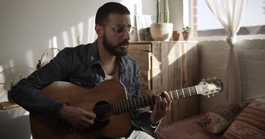 The man is playing guitar by the couch