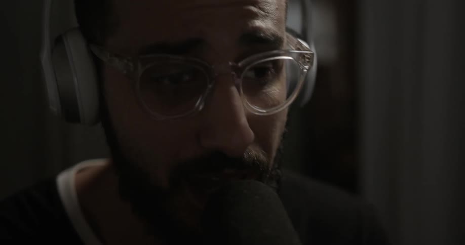 Man wearing headphones is singing into a microphone indoor