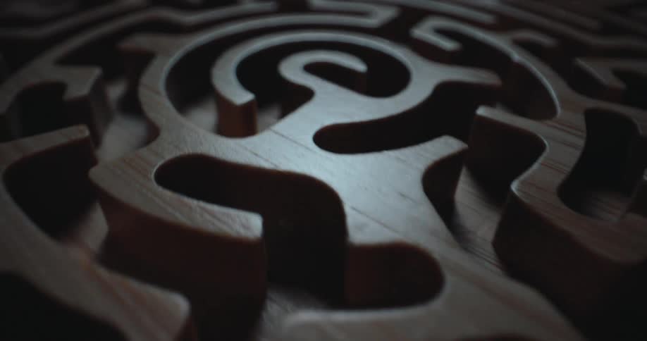 A classic wooden labyrinth maze game in a dark room with light reflecting off the wood