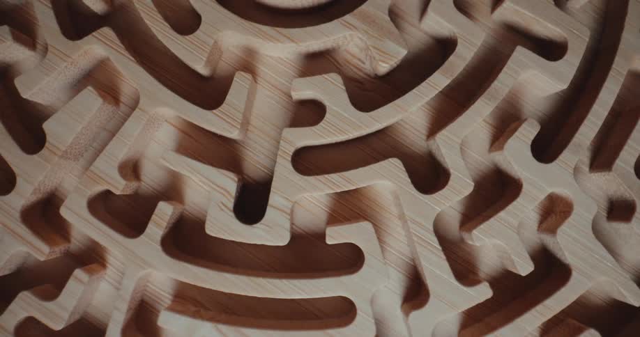 An overhead shot shows a circular wooden maze rotating slowly revealing intricate carved paths and deep shadows within the grain of the lightcolored timber as it spins around a central point