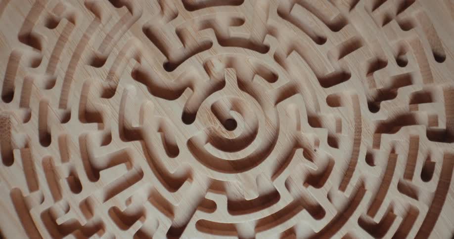 A close view of a carved wooden maze with intricate circular paths and smooth grain textures under changing light